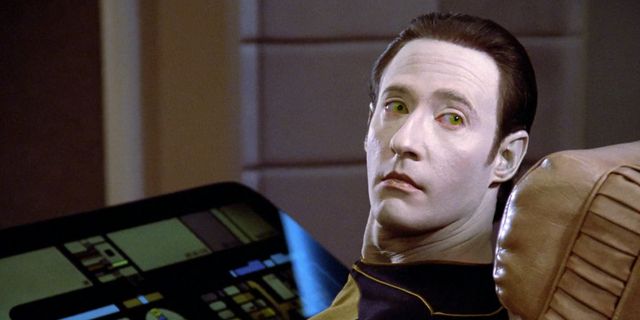 Data, the android from Star Trek TNG, sitting at the console and looking back at the camera with golden eyes

